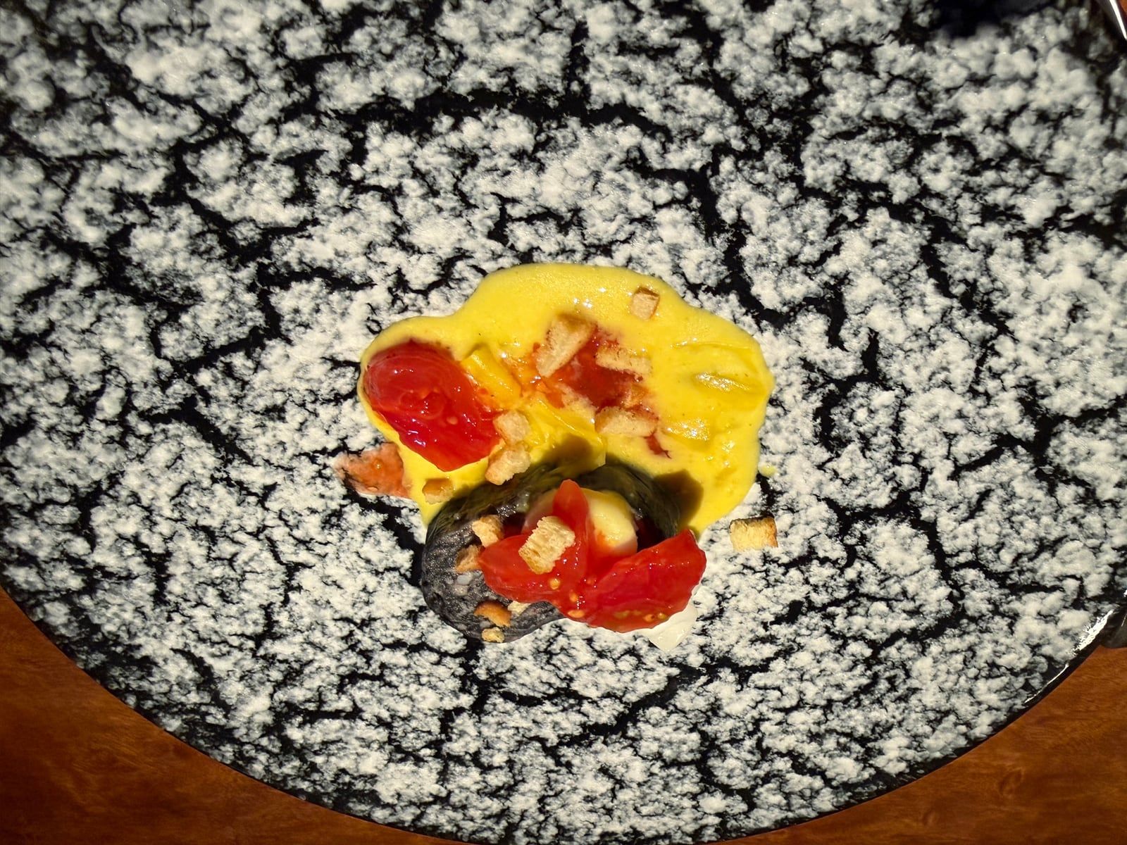 黒い皿に黄色いソースとトマトを合わせた料理