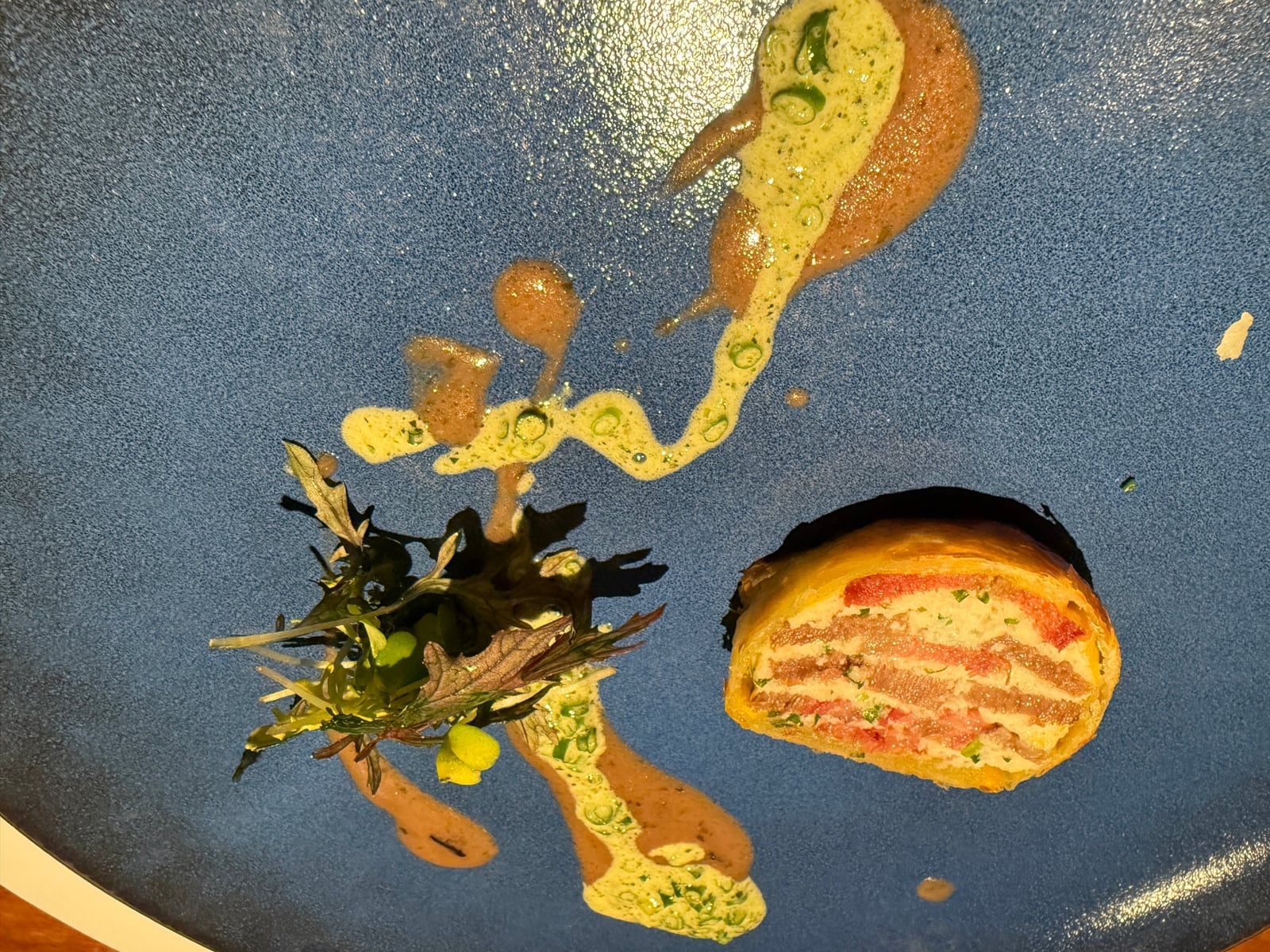 青い皿にパイ包みと二色のソースを盛った料理