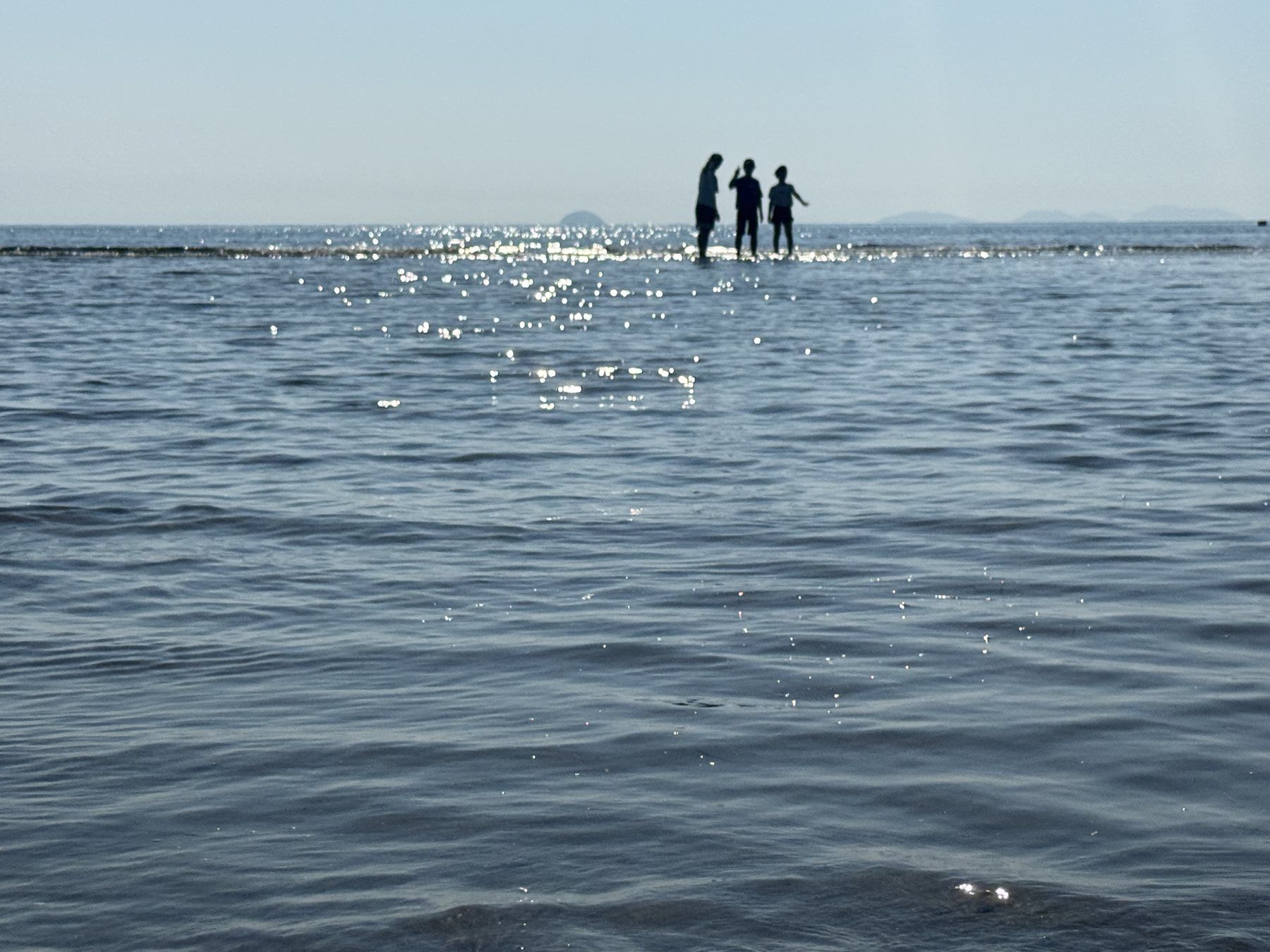 父母ヶ浜の遠浅の海を歩く家族のシルエット