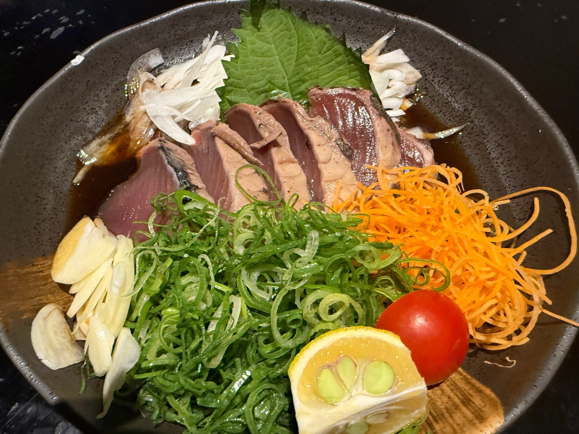 厚く切ったカツオのたたきにねぎ、にんにく、すだちが添えられた料理